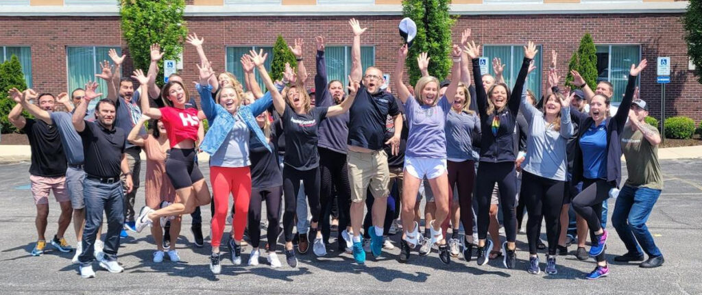 Team photo of employees jumping and waving at the camera in the parking lot.