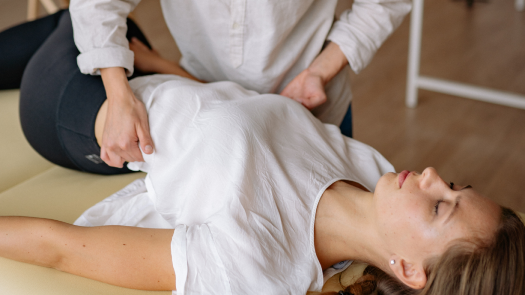 A person lying relaxed on a chiropractic table, positioned with their hips and knees turned to the right and their upper body flat, as they receive an adjustment.