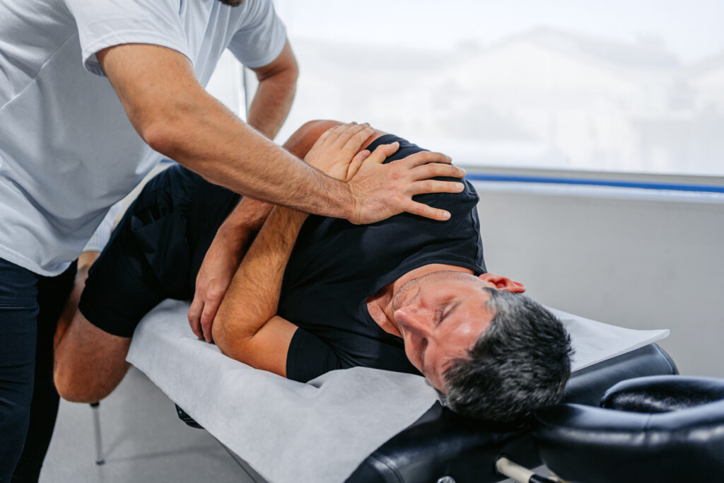 A chiropractor adjusting a patient's hips and lower back while the patient is lying on their side, facing the chiropractor.