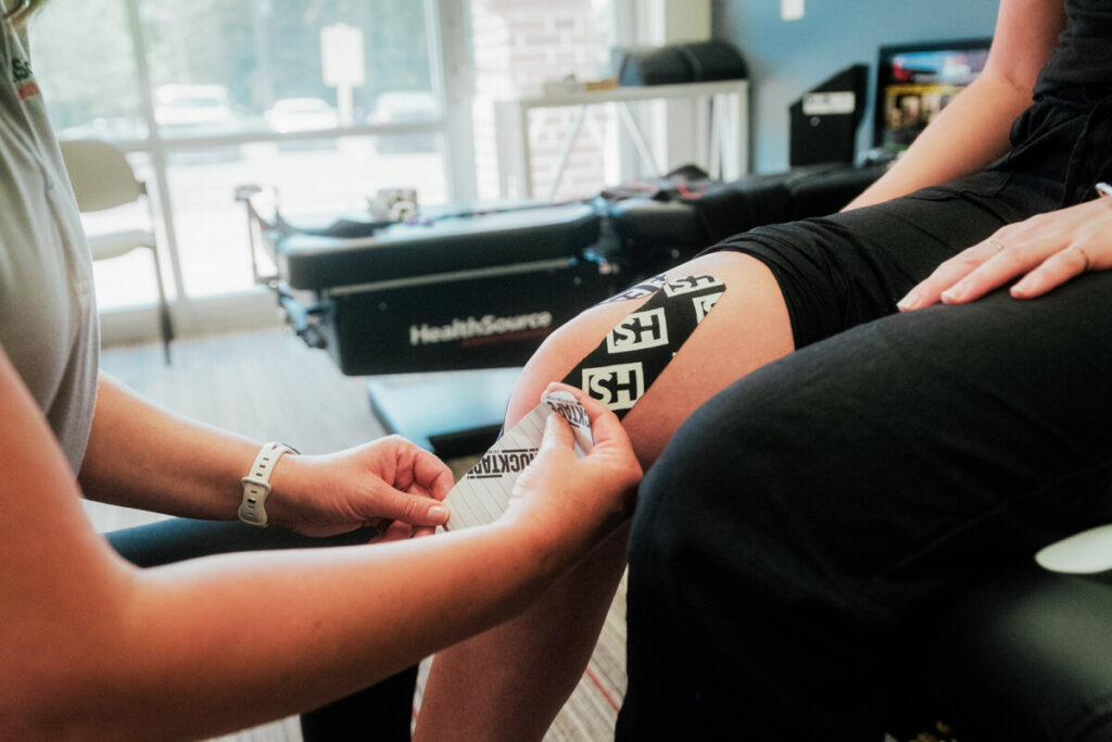 A HealthSource Rehabilitation Specialist applying black kinesiology tape to a patient's knee