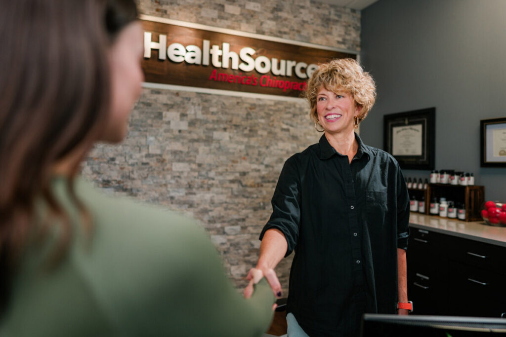 A friendly HealthSource team member smiles, greeting a patient at the front desk