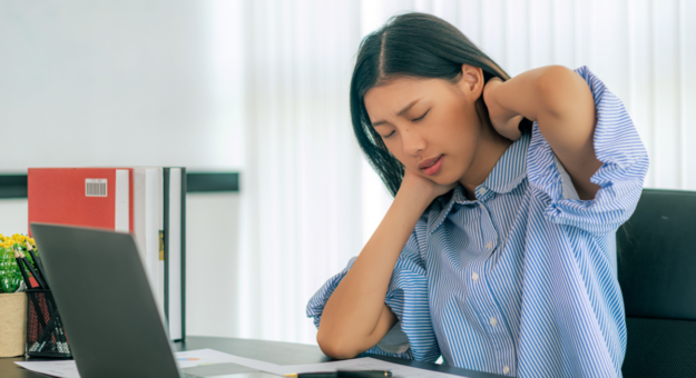 Woman experiencing tech neck sits at an office desk in front of a computer in pain.