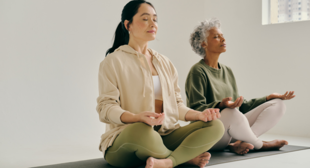 Two women sharing a yoga mat while practicing yoga on the floor