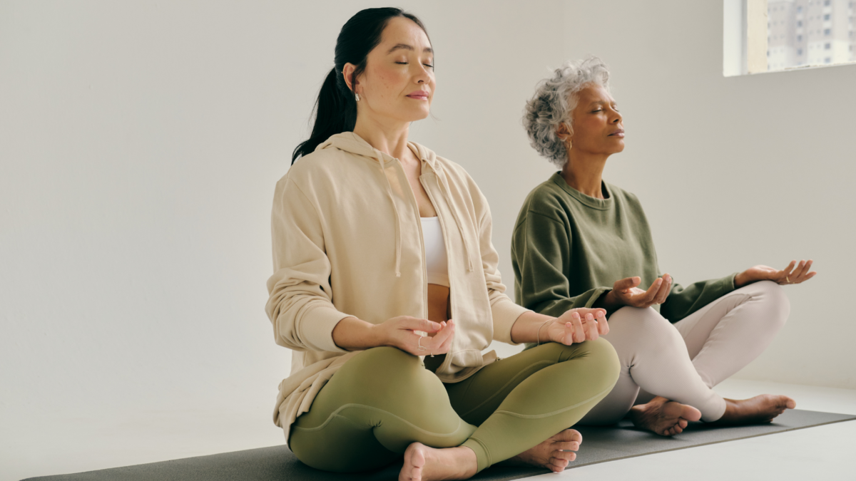 Two women sharing a yoga mat while practicing yoga on the floor