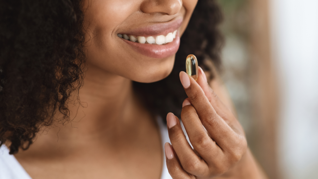 A woman smiling as she holds a supplement capsule near her mouth, preparing to take it. 